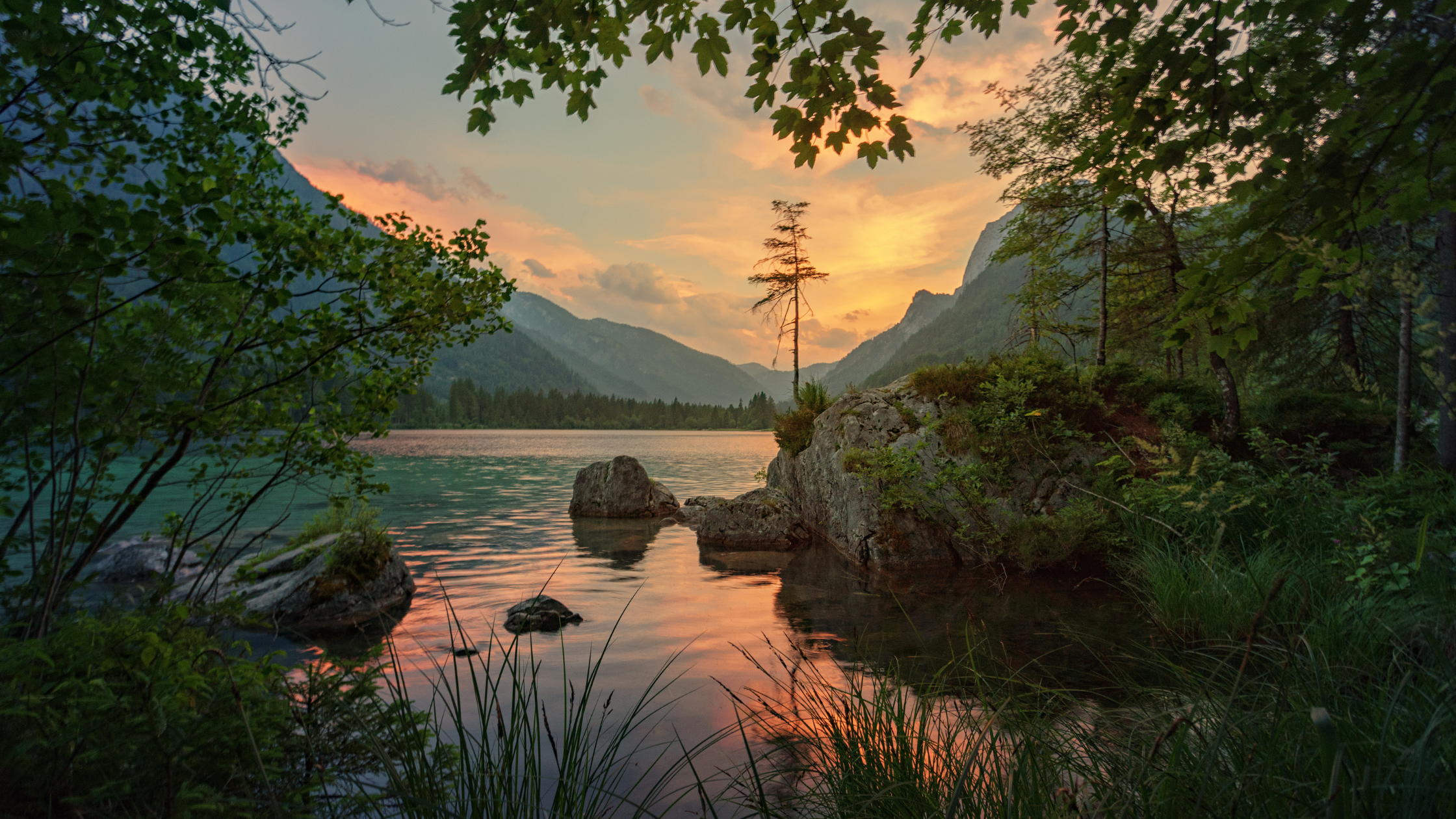 Image of a sunset on the lake with mountains and trees around